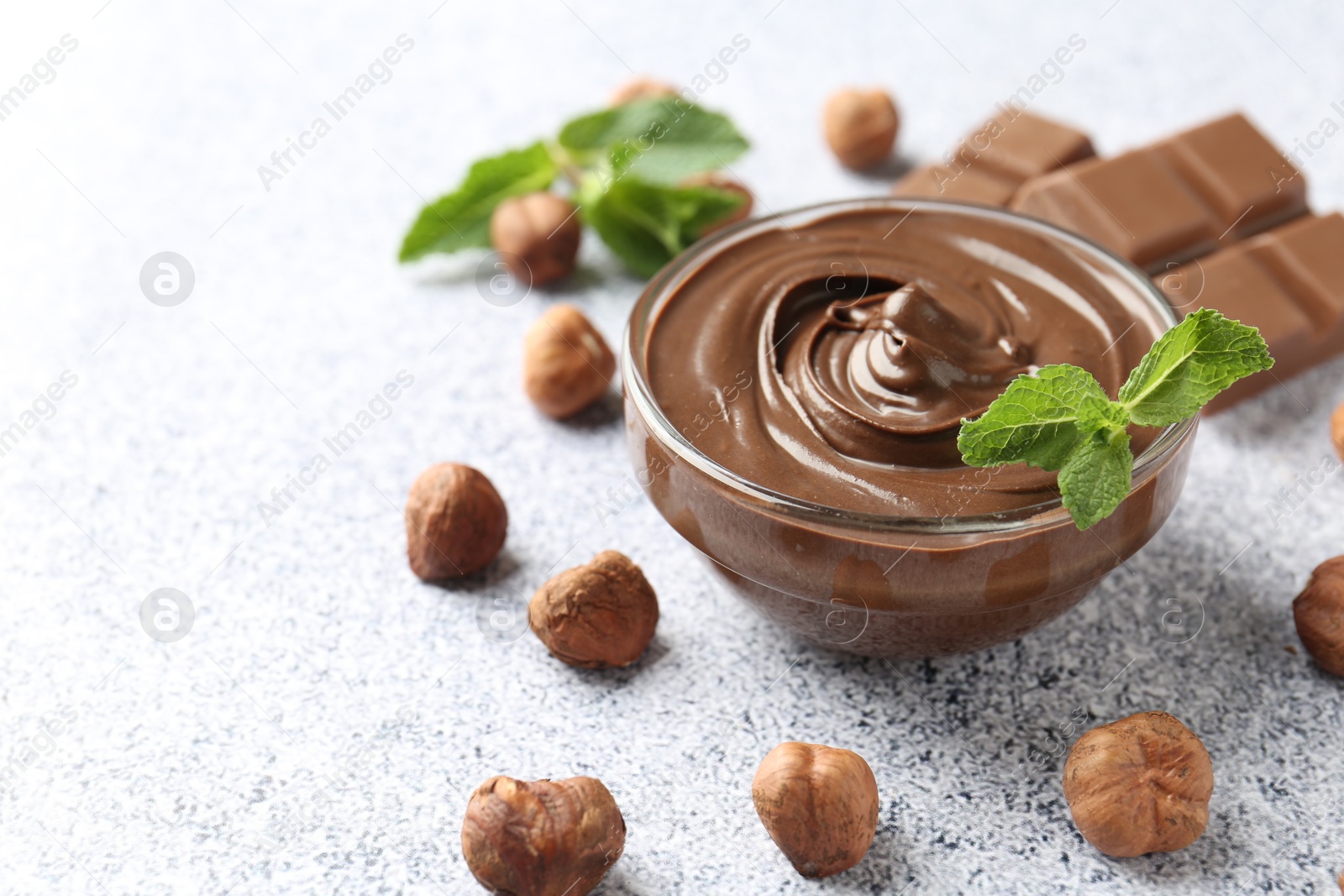 Photo of Tasty chocolate spread with mint in bowl and hazelnuts on grey textured table, closeup. Space for text