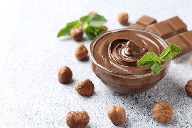 Photo of Tasty chocolate spread with mint in bowl and hazelnuts on grey textured table, closeup. Space for text
