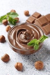 Photo of Tasty chocolate spread with mint in bowl and hazelnuts on grey textured table, closeup