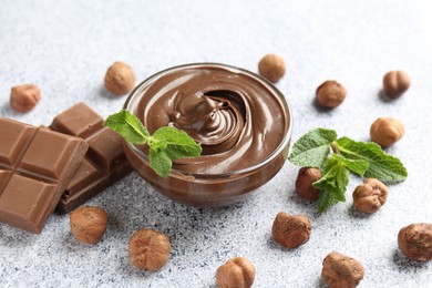 Photo of Tasty chocolate spread with mint in bowl and hazelnuts on grey textured table, closeup