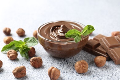 Photo of Tasty chocolate spread with mint in bowl and hazelnuts on grey textured table, closeup