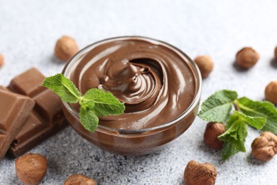 Photo of Tasty chocolate spread with mint in bowl and hazelnuts on grey textured table, closeup