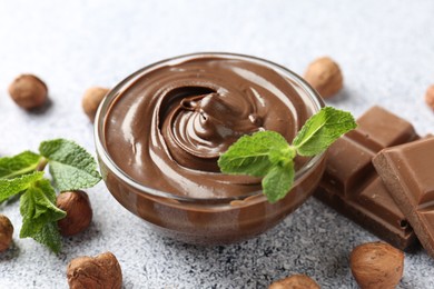Photo of Tasty chocolate spread with mint in bowl and hazelnuts on grey textured table, closeup