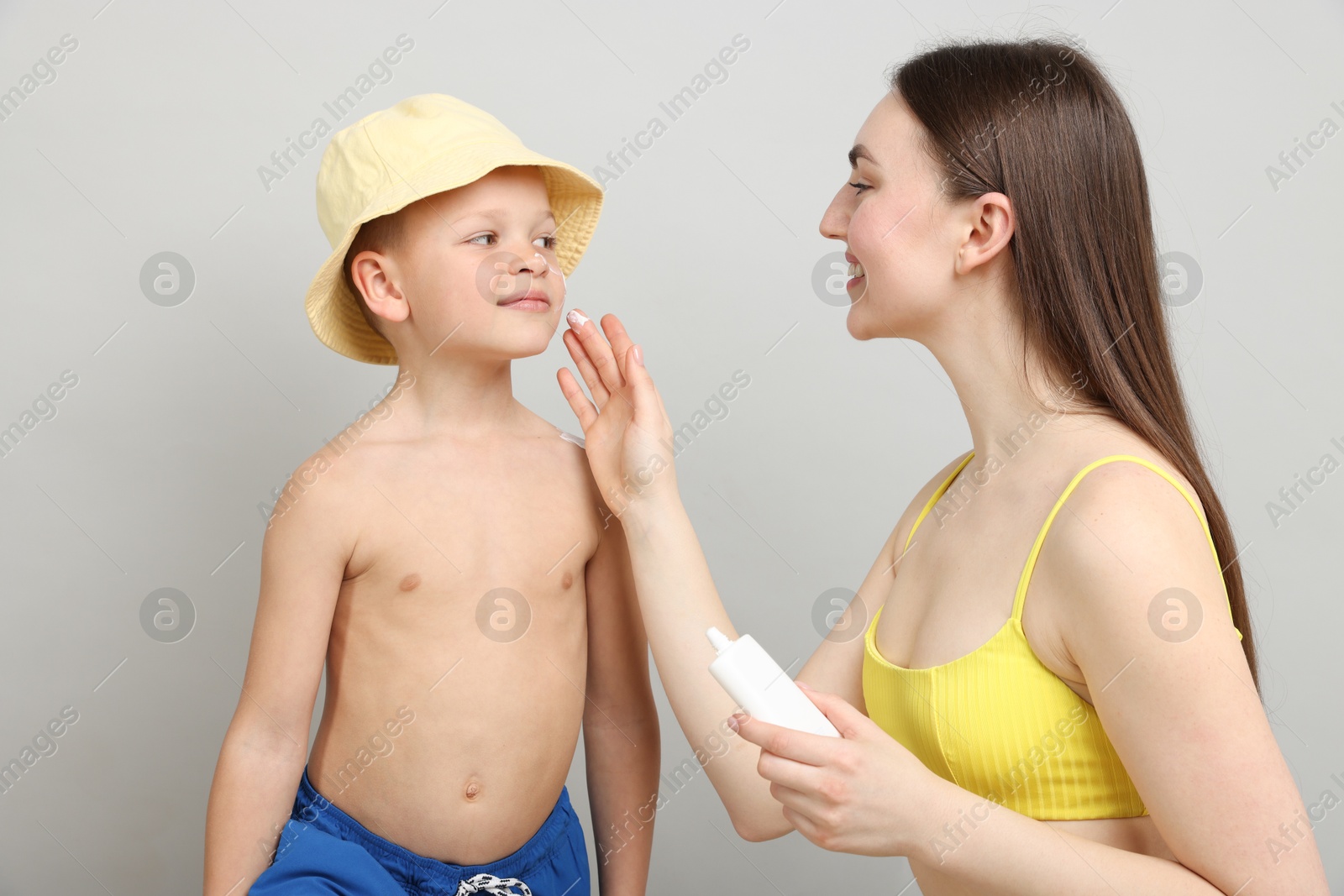 Mother applying sun protection cream onto her son's skin on light grey background Photo of Mother applying sun protection cream onto her son's skin on light grey background