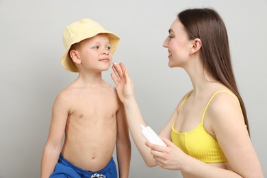 Photo of Mother applying sun protection cream onto her son's skin on light grey background