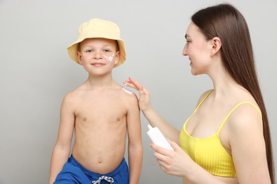 Photo of Mother applying sun protection cream onto her son's skin on light grey background