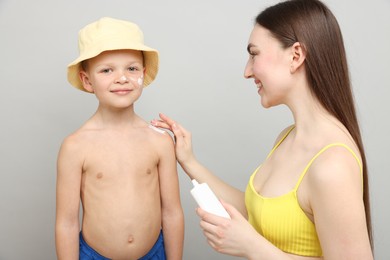 Photo of Mother applying sun protection cream onto her son's skin on light grey background