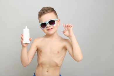 Photo of Little boy with tube of sun protection cream on light grey background