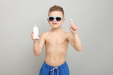 Photo of Little boy with tube of sun protection cream on light grey background