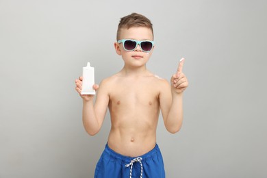 Photo of Little boy with tube of sun protection cream on light grey background