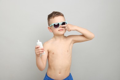 Photo of Little boy with tube applying sun protection cream onto his skin on light grey background