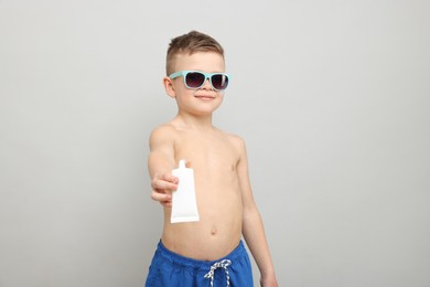 Photo of Little boy with tube of sun protection cream on light grey background