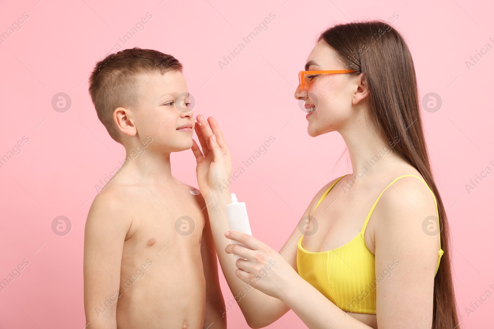 Mother applying sun protection cream onto her son's skin on pink background Photo of Mother applying sun protection cream onto her son's skin on pink background