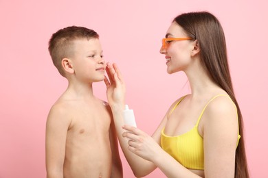 Photo of Mother applying sun protection cream onto her son's skin on pink background