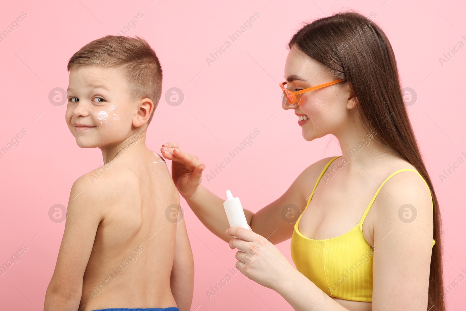 Mother applying sun protection cream onto her son's skin on pink background Photo of Mother applying sun protection cream onto her son's skin on pink background