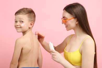 Photo of Mother applying sun protection cream onto her son's skin on pink background