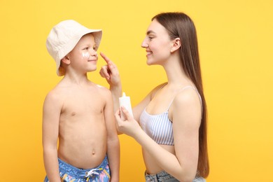 Photo of Mother applying sun protection cream onto her son's skin on yellow background