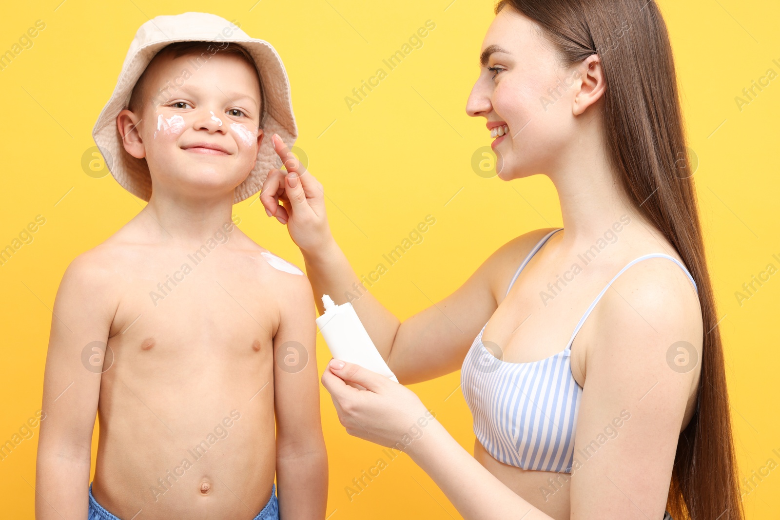 Mother applying sun protection cream onto her son's skin on yellow background Photo of Mother applying sun protection cream onto her son's skin on yellow background