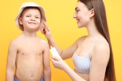 Photo of Mother applying sun protection cream onto her son's skin on yellow background