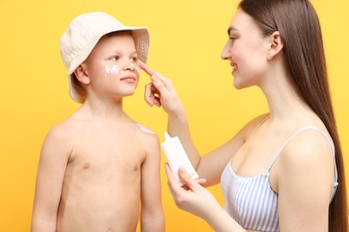 Photo of Mother applying sun protection cream onto her son's skin on yellow background
