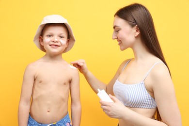 Photo of Mother applying sun protection cream onto her son's skin on yellow background