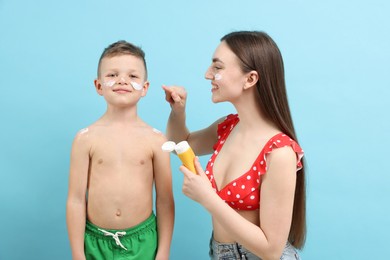 Photo of Mother applying sun protection cream onto her son's skin on light blue background