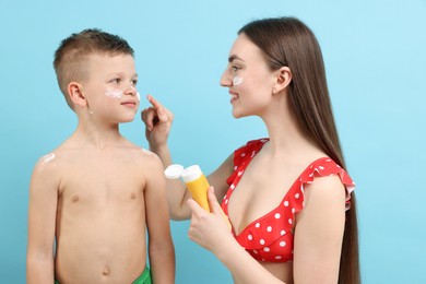 Photo of Mother applying sun protection cream onto her son's skin on light blue background