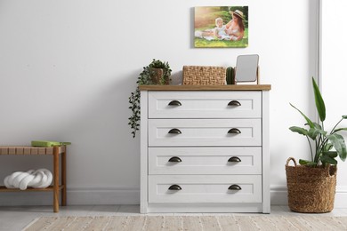 Photo of Dresser with stylish decor and houseplants near white wall indoors