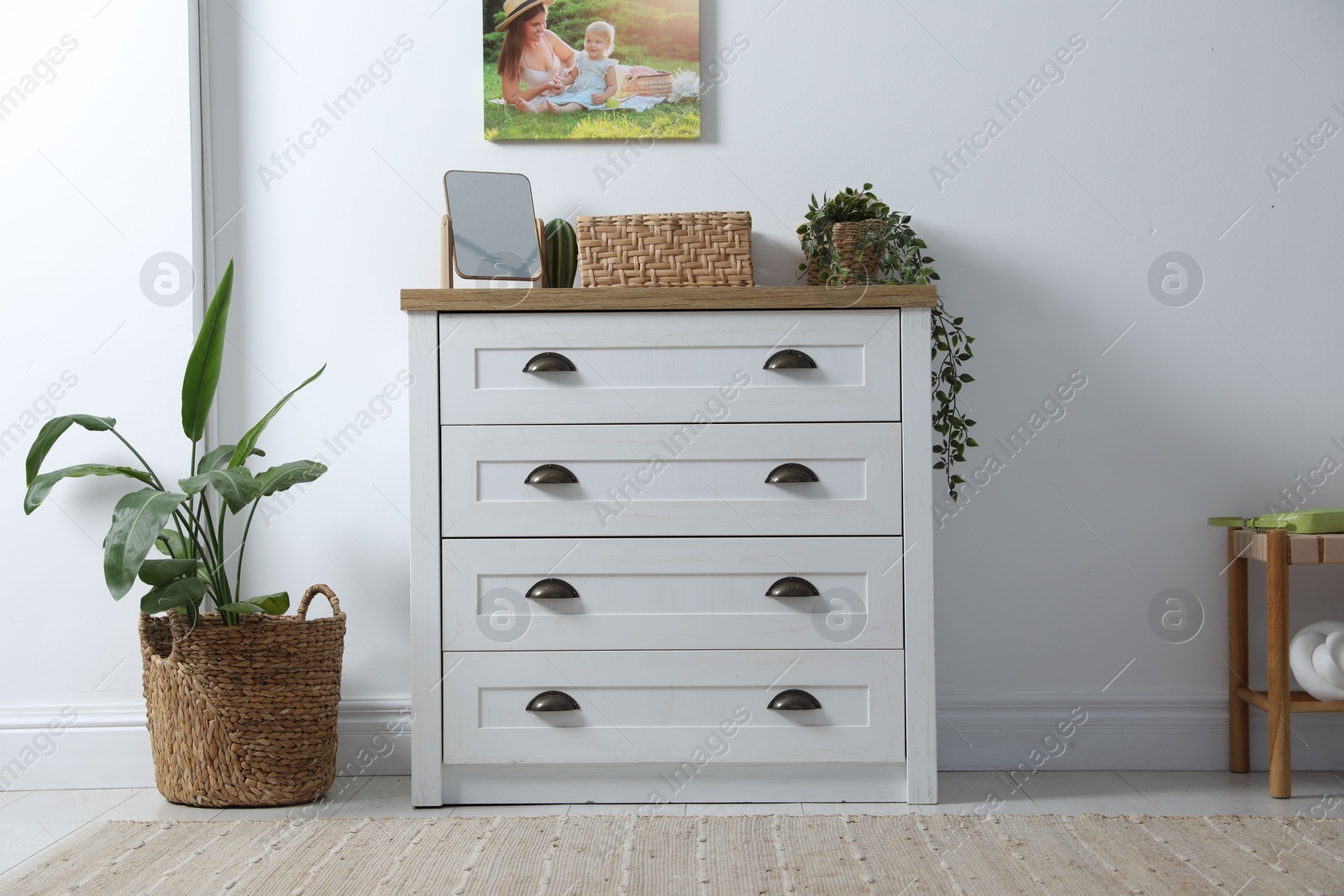 Dresser with stylish decor and houseplants near white wall indoors Photo of Dresser with stylish decor and houseplants near white wall indoors