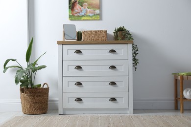 Photo of Dresser with stylish decor and houseplants near white wall indoors