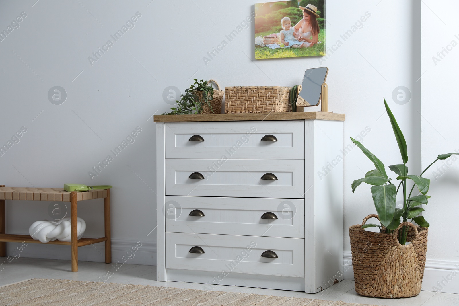 Dresser with stylish decor and houseplants near white wall indoors Photo of Dresser with stylish decor and houseplants near white wall indoors