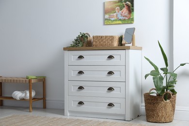 Photo of Dresser with stylish decor and houseplants near white wall indoors