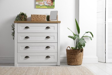 Photo of Dresser with stylish decor and houseplants near white wall indoors