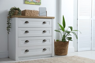 Photo of Dresser with stylish decor and houseplants near white wall indoors
