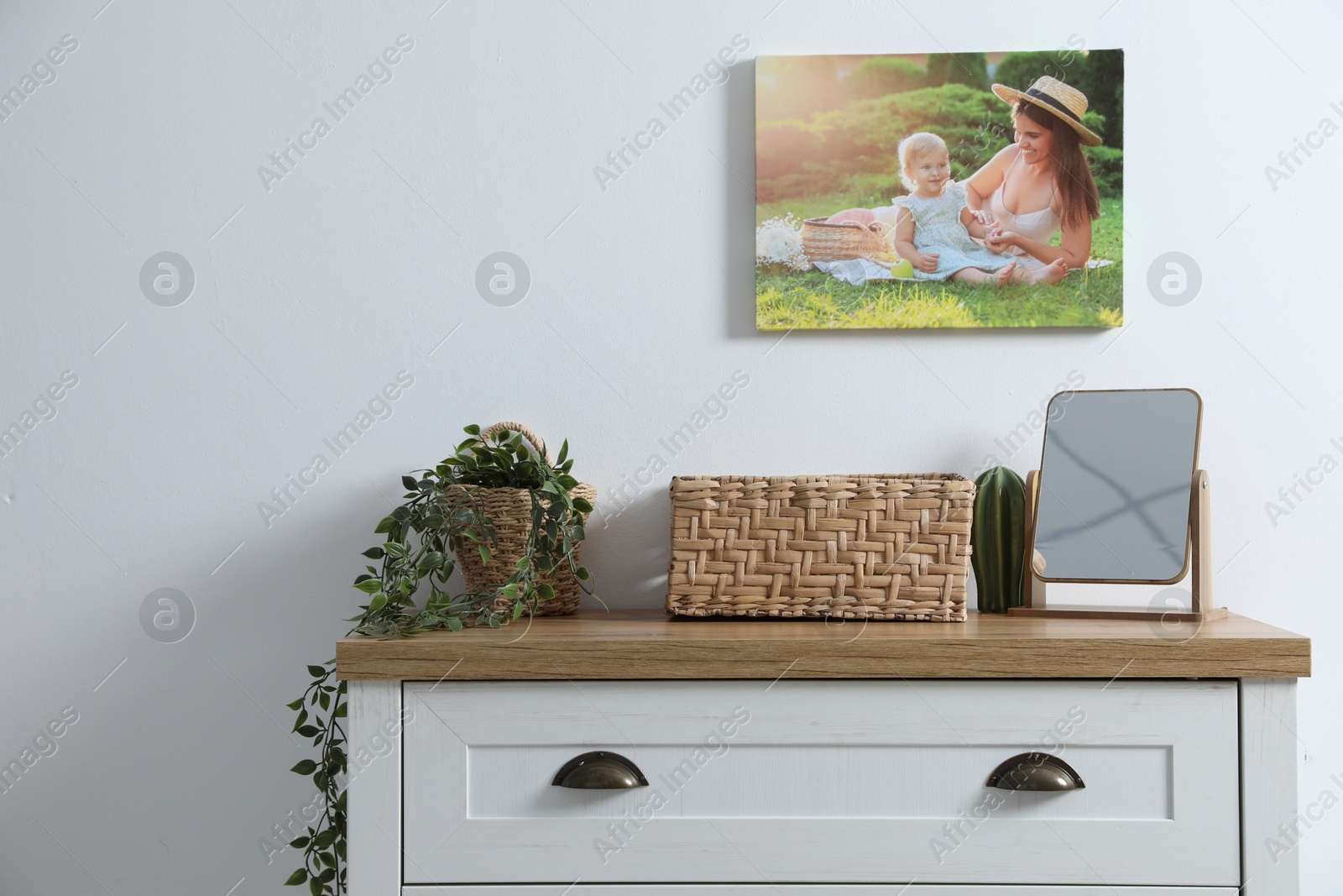 Dresser with stylish wicker basket, mirror and houseplant near white wall indoors Photo of Dresser with stylish wicker basket, mirror and houseplant near white wall indoors