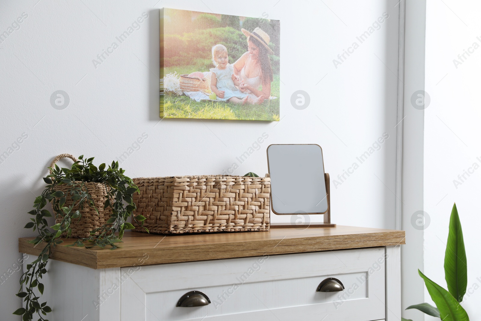 Dresser with stylish wicker basket, mirror and houseplant near white wall indoors Photo of Dresser with stylish wicker basket, mirror and houseplant near white wall indoors