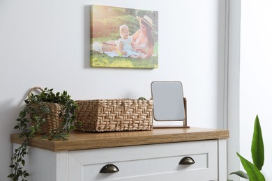 Photo of Dresser with stylish wicker basket, mirror and houseplant near white wall indoors