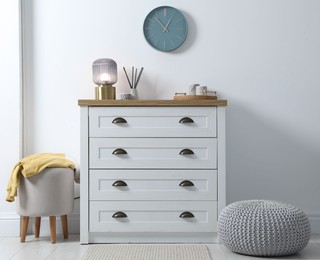 Photo of Dresser with stylish reed diffuser and lamp near white wall indoors