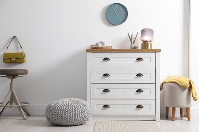 Photo of Dresser with stylish reed diffuser and lamp near white wall indoors