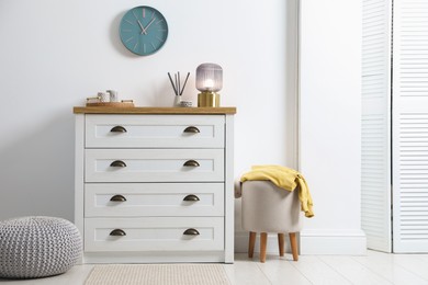 Photo of Dresser with stylish reed diffuser and lamp near white wall indoors