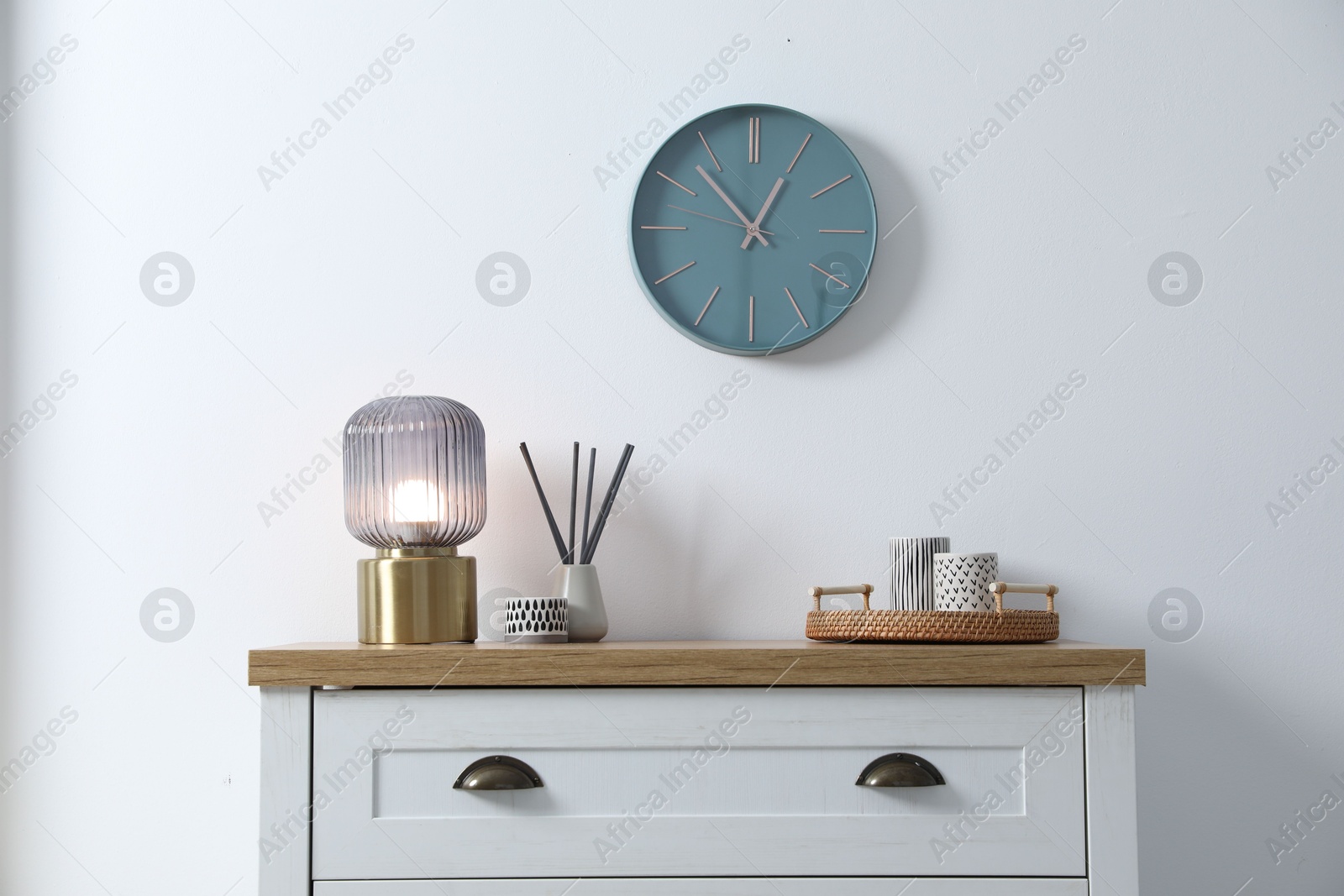 Dresser with stylish reed diffuser and lamp near white wall indoors Photo of Dresser with stylish reed diffuser and lamp near white wall indoors