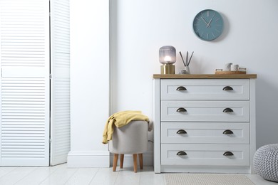 Photo of Dresser with stylish reed diffuser and lamp near white wall indoors