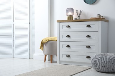 Photo of Dresser with stylish reed diffuser and lamp near white wall indoors