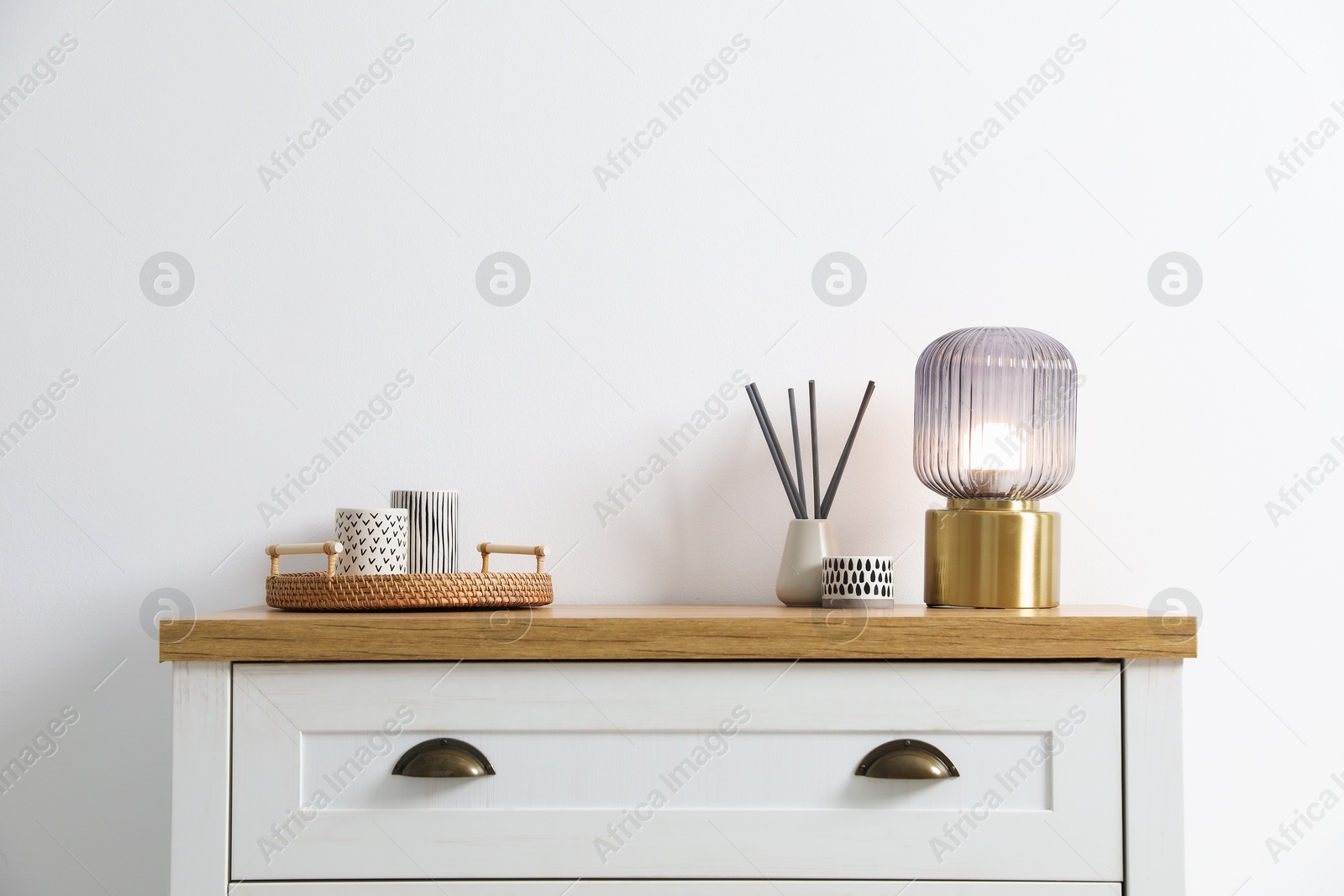 Dresser with stylish reed diffuser and lamp near white wall indoors Photo of Dresser with stylish reed diffuser and lamp near white wall indoors