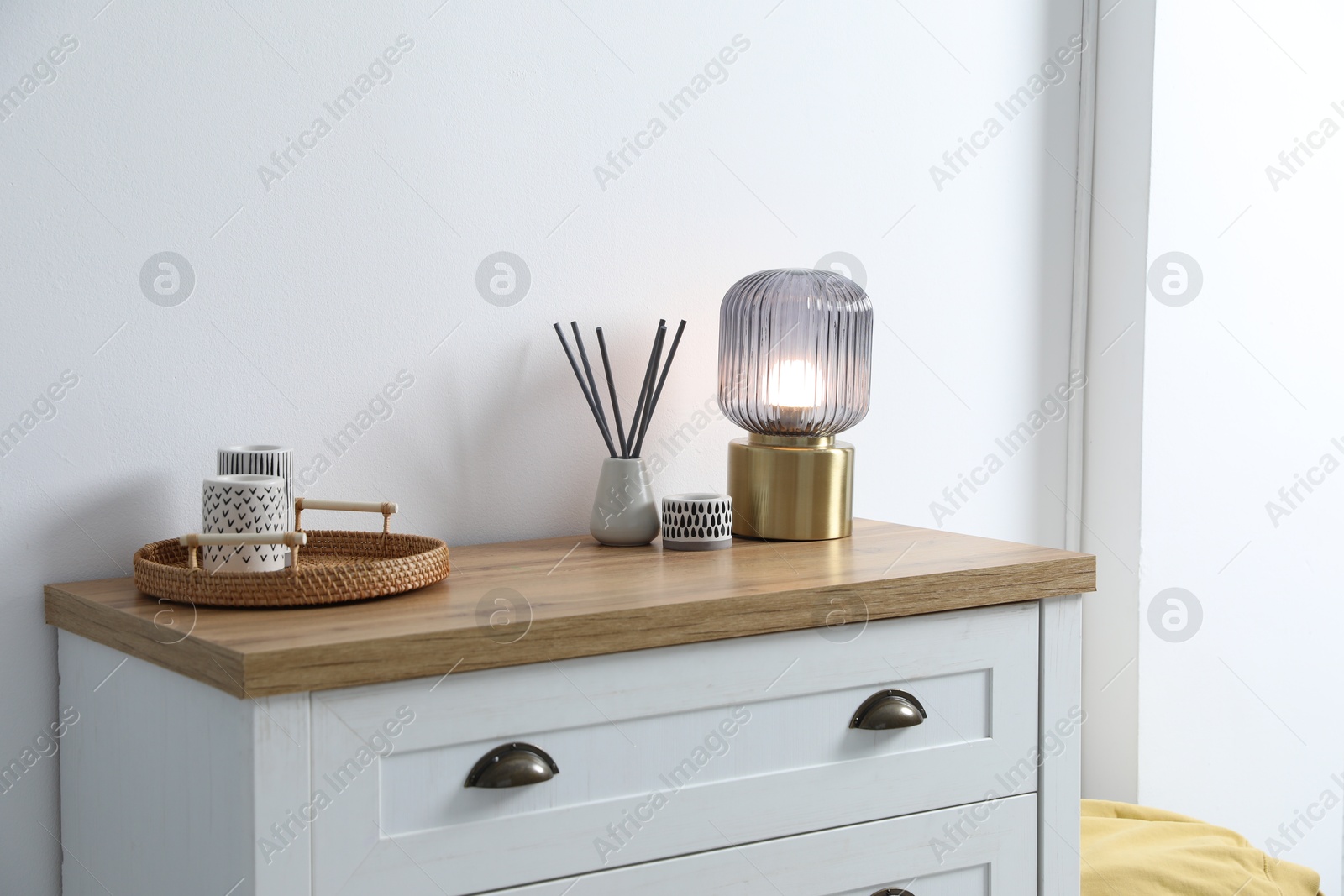 Dresser with stylish reed diffuser and lamp near white wall indoors Photo of Dresser with stylish reed diffuser and lamp near white wall indoors