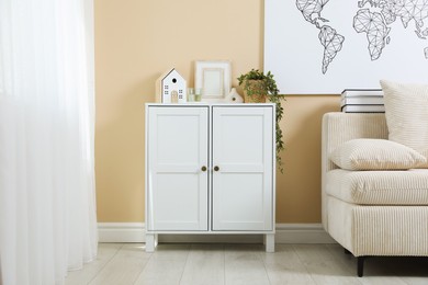 Photo of Dresser with stylish decor and houseplant near beige wall indoors
