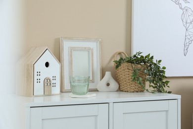 Photo of Dresser with stylish decor and houseplant near beige wall indoors