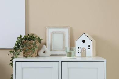 Photo of Dresser with stylish decor and houseplant near beige wall indoors
