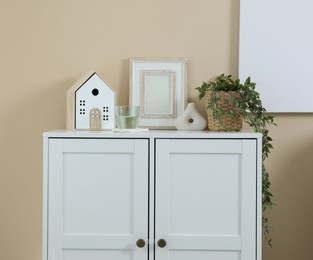 Photo of Dresser with stylish decor and houseplant near beige wall indoors