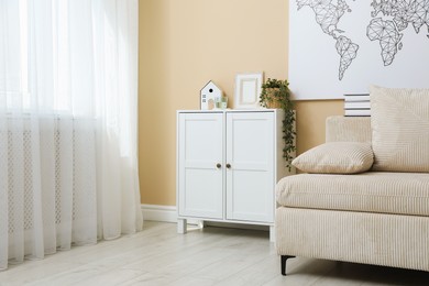Photo of Dresser with stylish decor and houseplant near beige wall in room